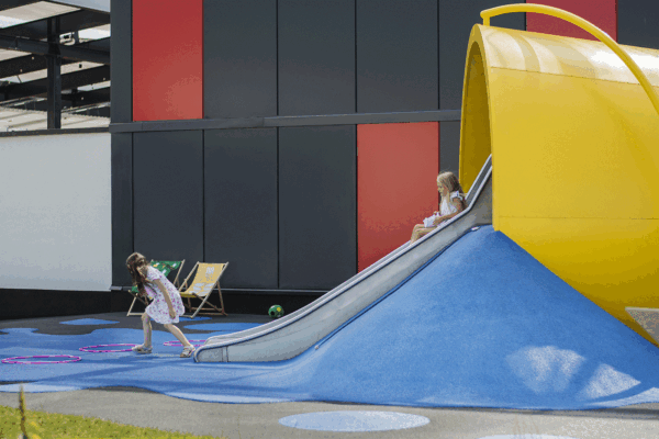 Art playground look like over size cup from which juice is spilling. It is a play sculpture with a slide and sandpit.